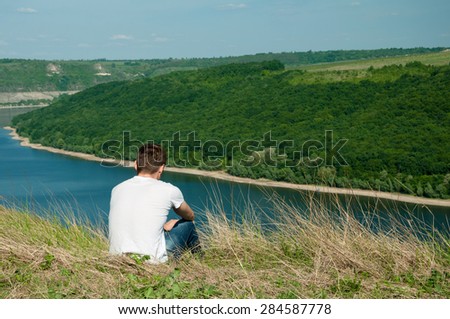 Young man sitting on a top of a mountain viewing wide river