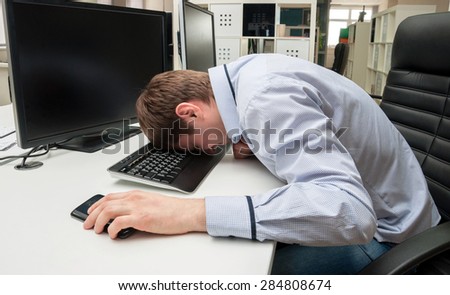 Young handsome man with computer in the office. Thinking over task in programming. Sleeping upon a keyboard