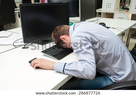 Young handsome man with computer in the office. Thinking over task in programming. Speeping upon a keyboard