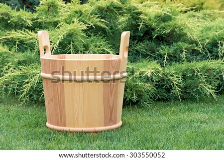 Wooden bucket for sauna in the green grass on a background of juniper.