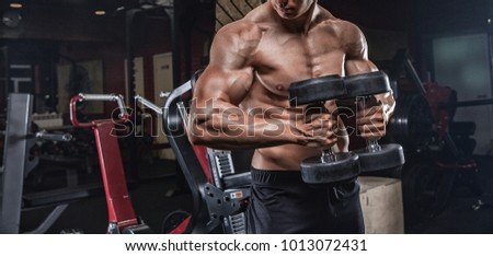 handsome man with big muscles trains in the gym, exercises for the development of the muscles of the hands, makes the lifting of dumbbells.