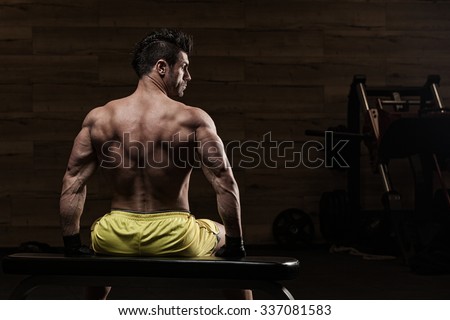 Muscle athlete man in gym making elevations. Bodybuilder training in gym