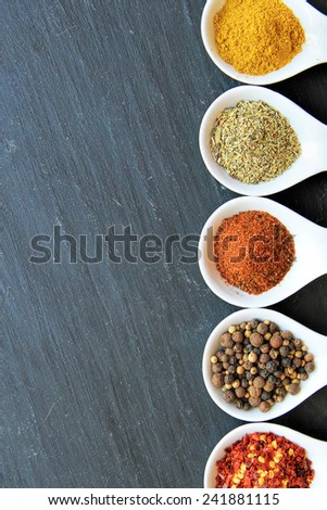 variety of spices on a black slice. From  up to down: curry powder, Provencal Herbs, paprika,  Black Peppercorn, espelette chili,
