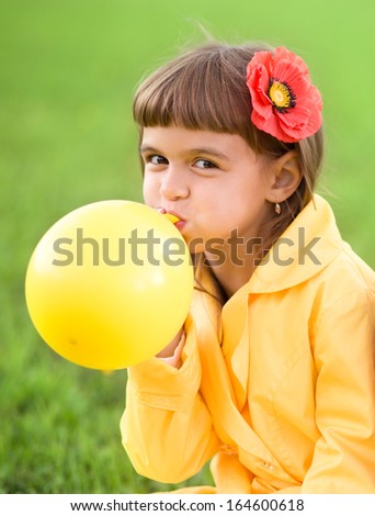 Little girl is inflating yellow balloon outdoors