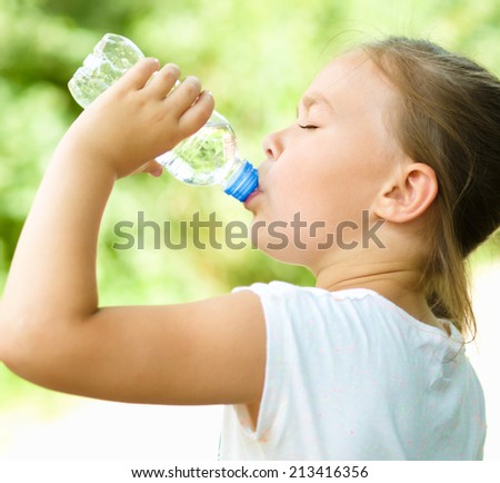 Cute little girl drinks water from a plastic bottle