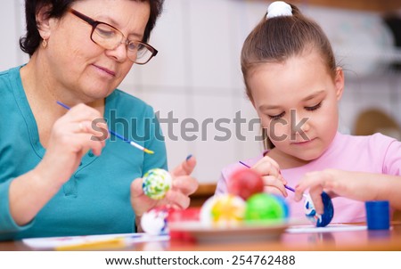 Grandmother with her granddaughter are coloring eggs for Easter, indoors