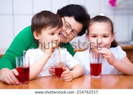 Grandmother with her grandchildren drink fruit juice, indoors