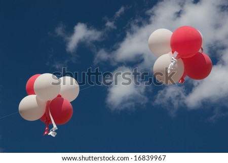 Red and white balloons with ribbons against blue sky.