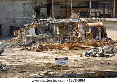Concrete rubble and crumpled machinery in demolished industrial plant, sign in foreground says \
