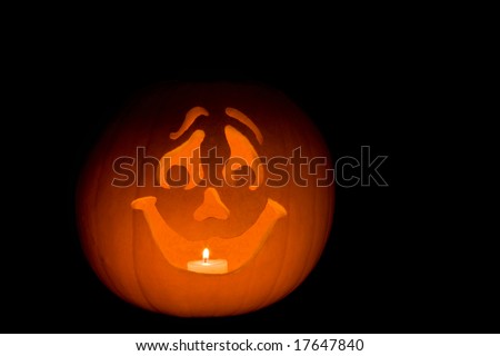 Carved pumpkin Jack-O-Lantern with happy face, candle burning inside, surrounded by black background
