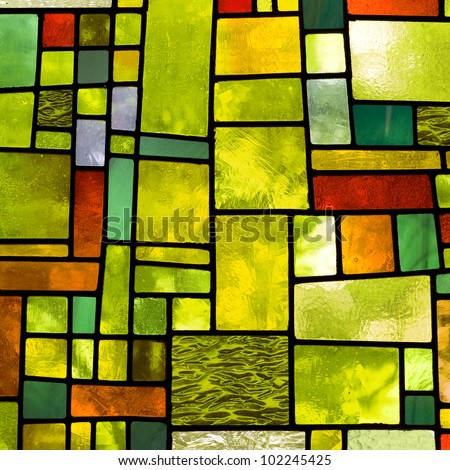 Image of a multicolored stained glass window with irregular block pattern in a hue of green, square format