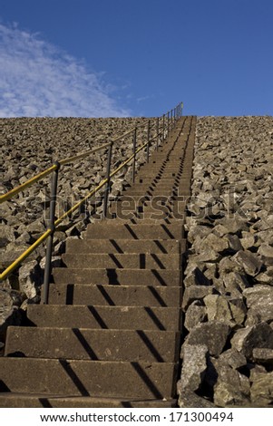 Concrete stairway with yellow handrail on rocky slope - square format