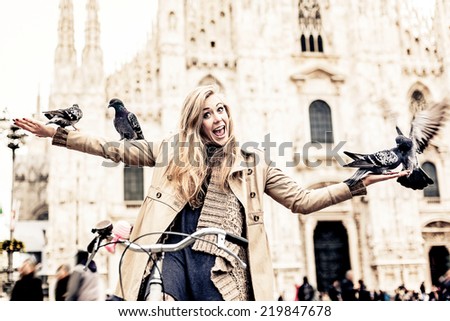 Woman sitting on her bicycle and playing with pigeons. Milan, Italy.