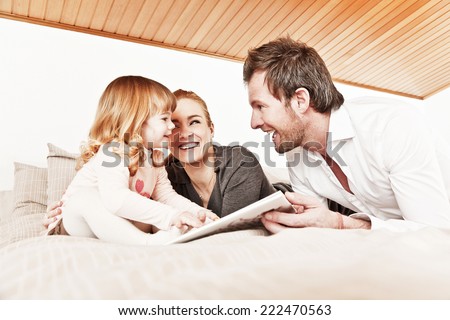 Mother, father and daughter reading a book together.