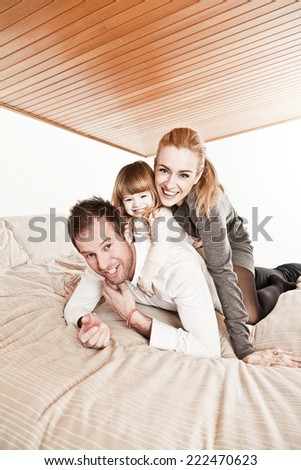Mother, father and daughter smiling on bed.