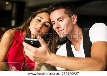 Beautiful Couple looking pics on mobile phone.