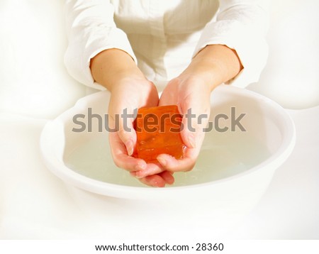 Hands holding a bar of transparent orange soap over a bowl of water. Very high key.