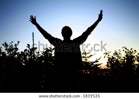 Young man raising his arms, silhouetted against the setting sun