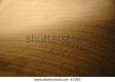 A picture of a stock market section of the paper which was captured under a golden shaded indoor light.