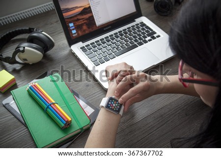 Prague, Czech Republic - January 23, 2016: Photo of women taping on Apple Watch at Home workplace with Apple Macbook Pro, iPad produced by Apple Computer, Inc..