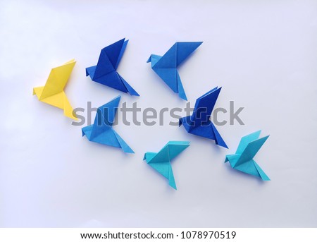 Seven blue origami  birds are flying leading by a yellow bird , isolated on white.