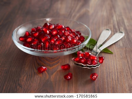 Fresh ripe pomegranate seeds on a glass plate. Wooden background
