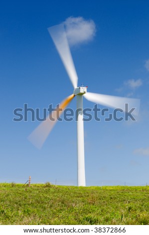Single wind turbine on grassy field over deep blue sky, alternative energy, green power, electricity generator. Long exposure to show spinning motion, blurred blades.