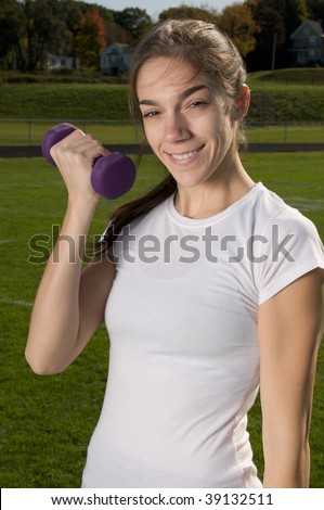 Young thin woman exercising outdoors, doing weight training with dumbbells