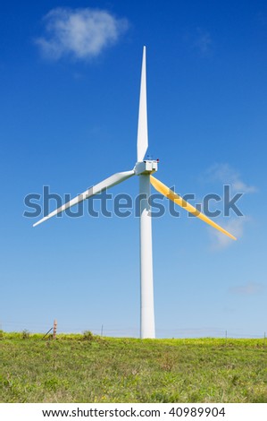 Single wind turbine on grassy field over deep blue sky, alternative energy, green power, electricity generator