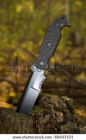 Black knife that is in a stump with a fall forest around