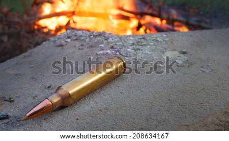 Rifle cartridge on a rock being warmed by a fire