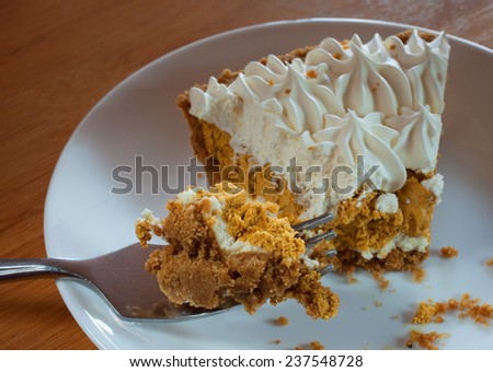 Big bite of pumpkin pie on a fork with a slice behind