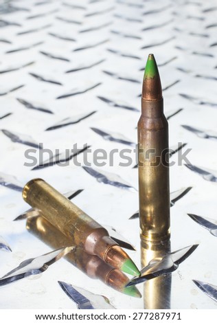 Rifle cartridges with green tipped bullets on a piece or armor plated metal