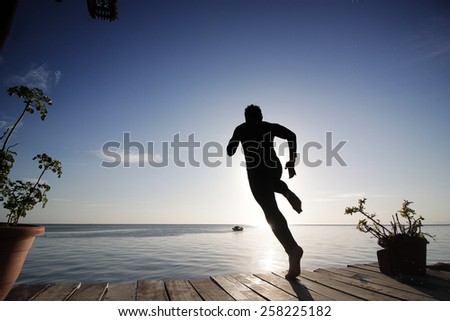 silhouette view of a man jump from a dock to the open sea water in sunset
