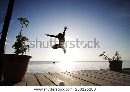 silhouette view of a man jump from a dock to the open sea water in sunset
