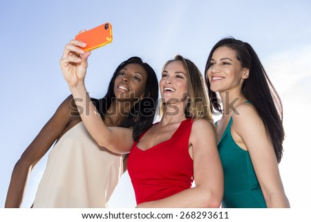 Portrait of three women taking selfies with a smartphone. Three friends posing for selfie, outdoors.