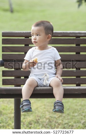 Cute Chinese baby boy eating bread in a park, shot in Beijing, China