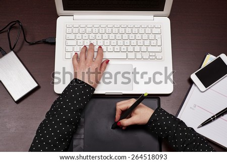Woman hands using graphic tablet on a desk with a phone and a diary