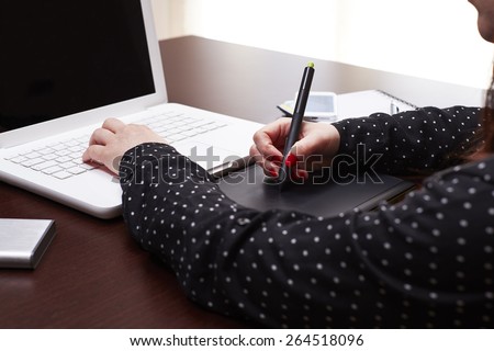Woman hands using graphic tablet on a desk with a phone and a diary