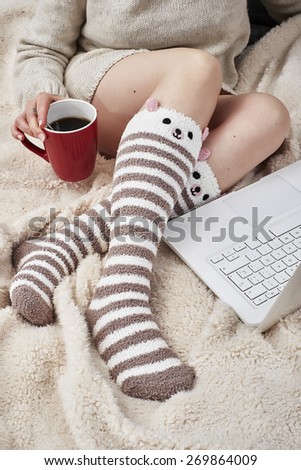 Woman on bed with bear socks and cup of coffee using a laptop