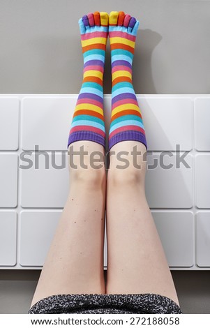 Woman legs raised up on bed wearing colorful socks.