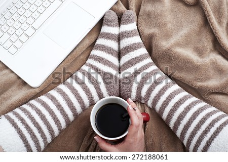 Woman on bed with bear socks and cup of coffee using a laptop