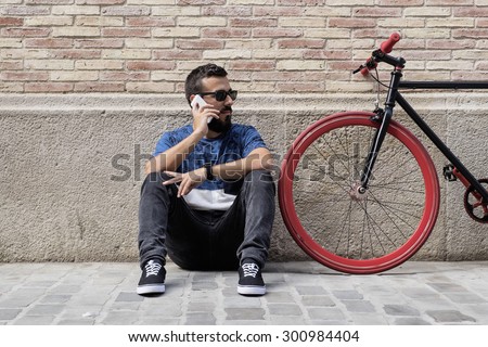 Young hipster man on the phone with his fixed bicycle on the wall