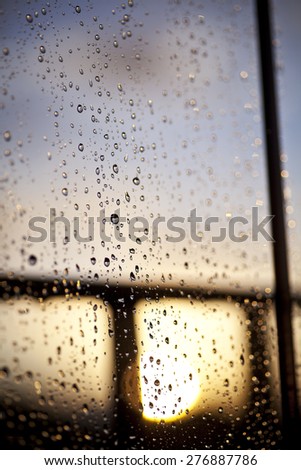 Rain drops on a window with the sun setting behind
