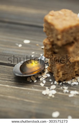 Stack of three pieces of flapjack on a wooden background. Scattering of rolled oats and a spoon full of golden syrup (two of the main ingredients in flapjacks)