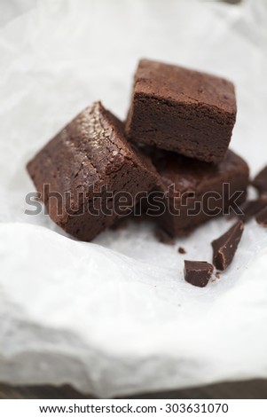 Stack of three pieces of chocolate brownie cake on crumpled white baking paper. Scattering of chocolate in the foreground