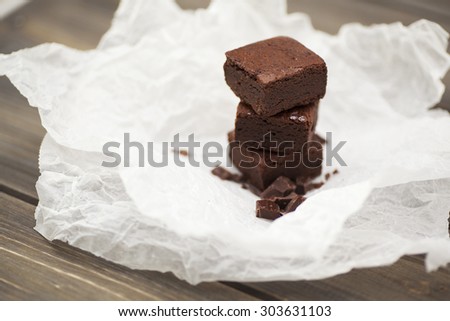 Stack of three pieces of chocolate brownie cake on a wooden background with crumpled white baking paper. Scattering of chocolate in the foreground