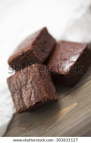 Stack of three pieces of chocolate brownie cake on a wooden background with crumpled white baking paper