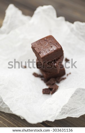 Stack of three pieces of chocolate brownie cake on a wooden background with crumpled white baking paper. Scattering of chocolate in the foreground