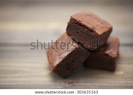 Stack of three pieces of chocolate brownie cake on a wooden background.